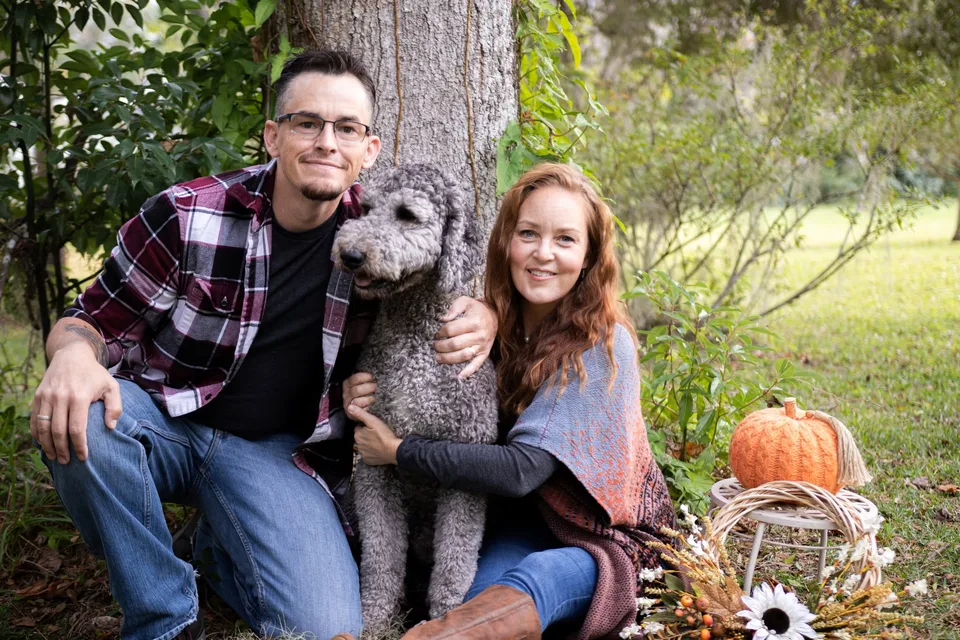 Two people sitting with a curly-haired dog outdoors.